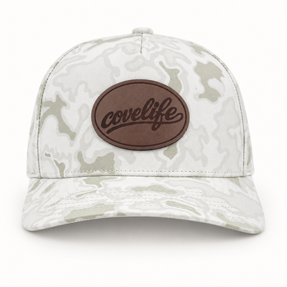 A structured baseball cap with a light gray and off-white camouflage pattern, featuring a brown oval patch on the front with the brand name 'covelife' in black script.