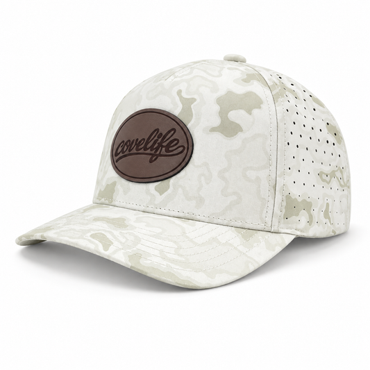 A baseball cap with a light beige and off-white camouflage pattern, featuring a brown oval patch on the front with the brand name 'covelife' in black script. The cap has perforated side panels for ventilation and is shown on a clean white background.