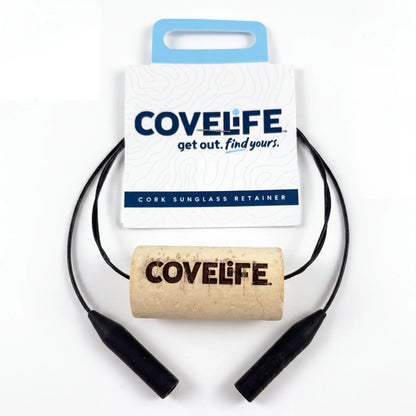 Cork sunglasses retainer with black cable cords and a natural cork center printed with the COVELIFE logo, displayed in front of its white and blue retail packaging card on a white background.