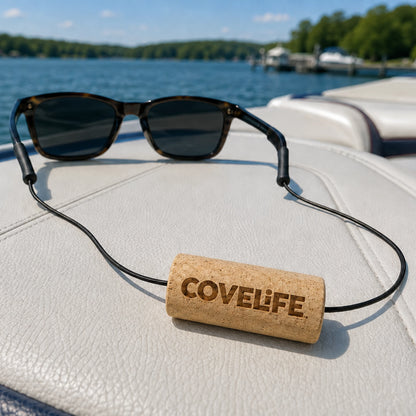 A pair of sunglasses with the  COVELIFE sunglass retainer resting on a white boat seat with a lake and trees in the background.
