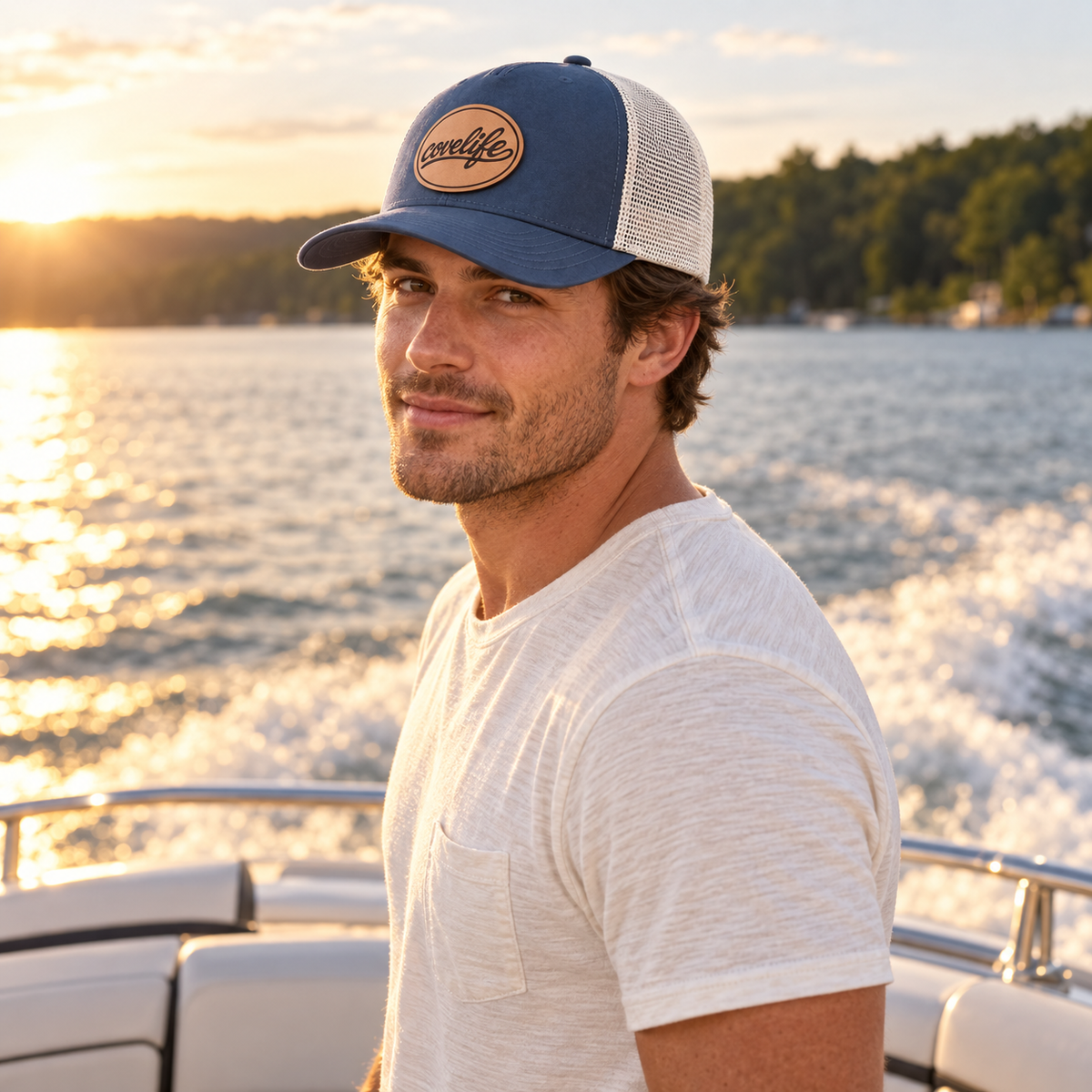 A man wearing the covelife classic mesh hat with covelife script heritage leather patch standing on a boat with water and a sunset in the background.
