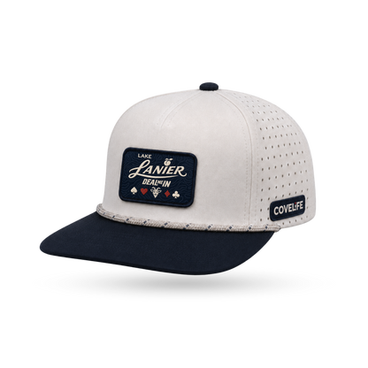 A premium structured baseball cap with a light cream crown, perforated side panels, and a dark navy flat brim. The front features a dark navy rectangular patch with white script reading LAKE LANIER DEAL ME IN", and the side displays a small black patch with 'COVELiFE' in white.