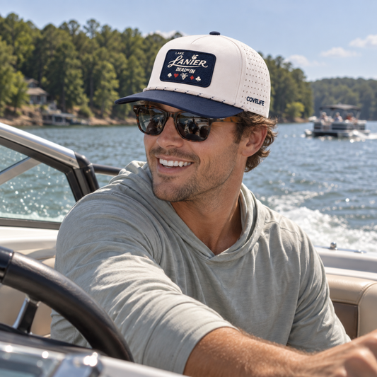 Man driving a boat on Lake Lanier wearing the COVELiFE DEAL ME IN cream and navy performance rope cap.